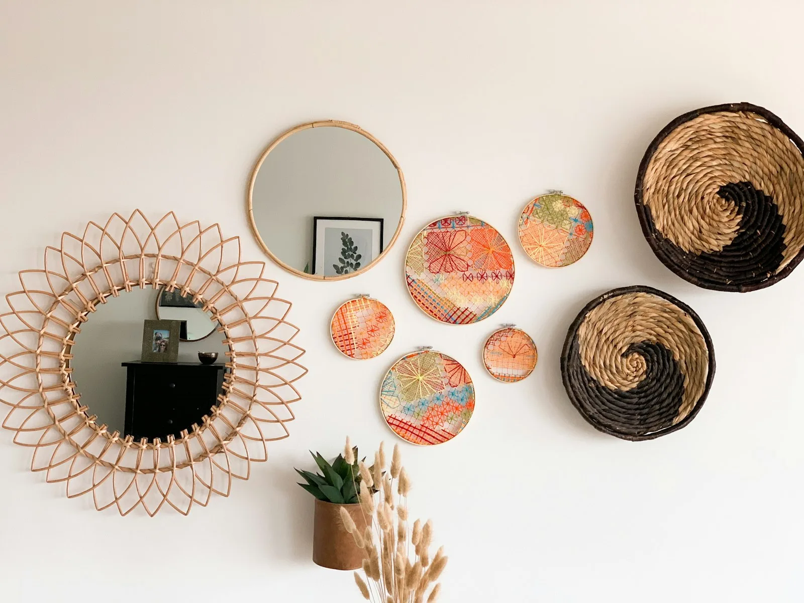 Wall display of woven baskets, a rattan mirror and colorful woven plates in warm tones