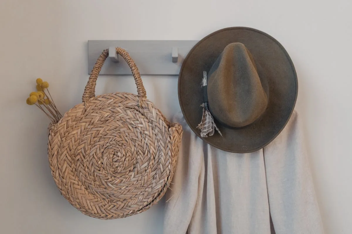 Wall hooks by a door holding a woven bag, hat and scarf in a small entryway