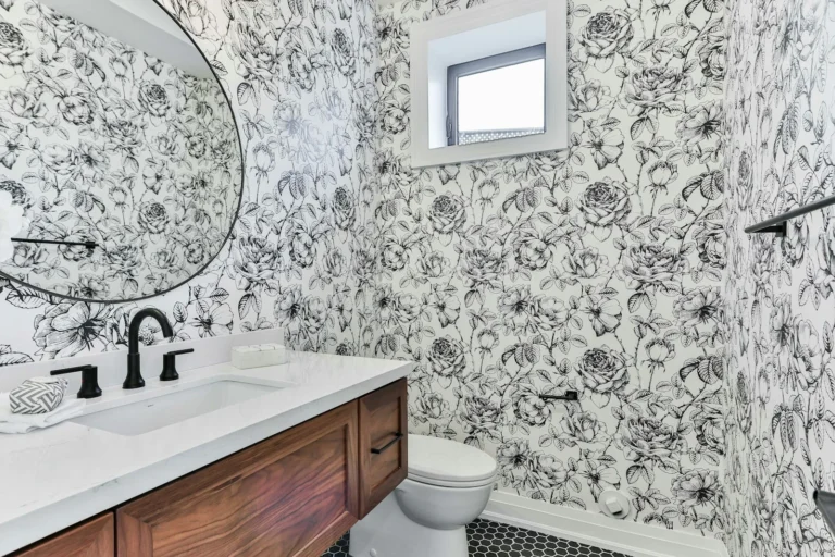 Small renter bathroom with floral peel-and-stick wallpaper covering the vanity wall and round mirror above a wood vanity