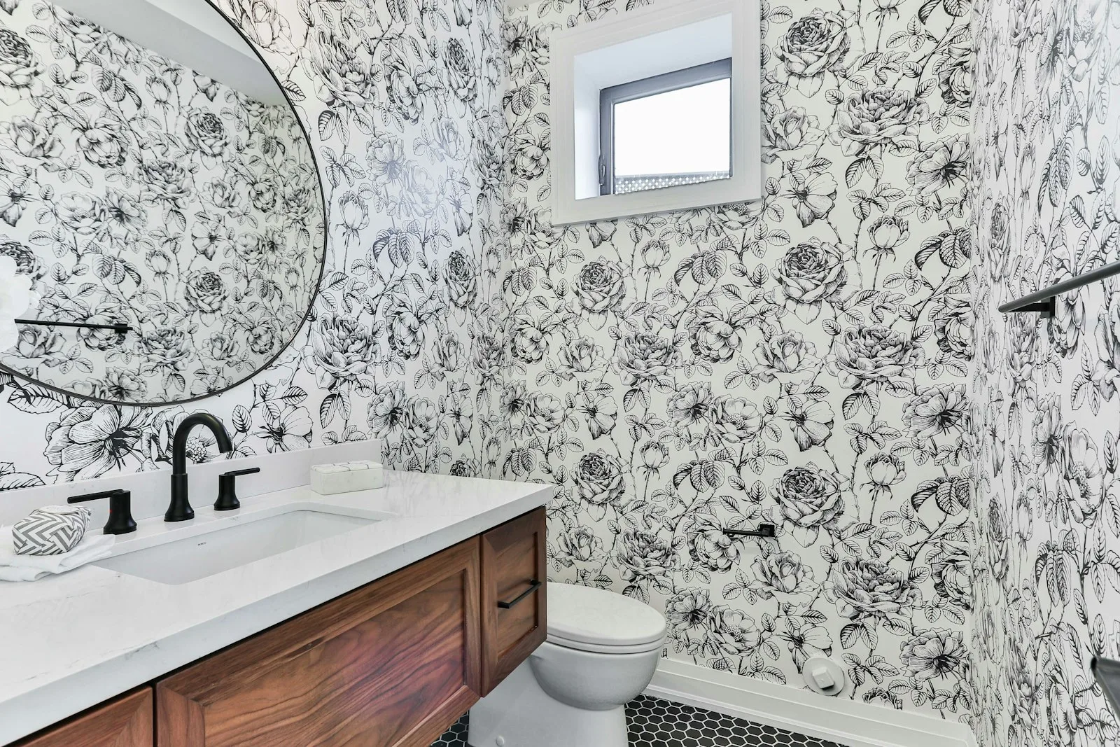 Small renter bathroom with floral peel-and-stick wallpaper covering the vanity wall and round mirror above a wood vanity