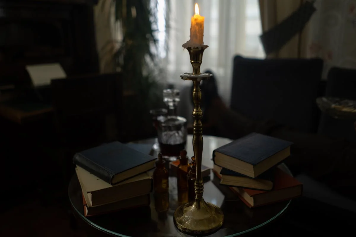 Brass candlestick with a lit candle beside stacked books on a dark side table