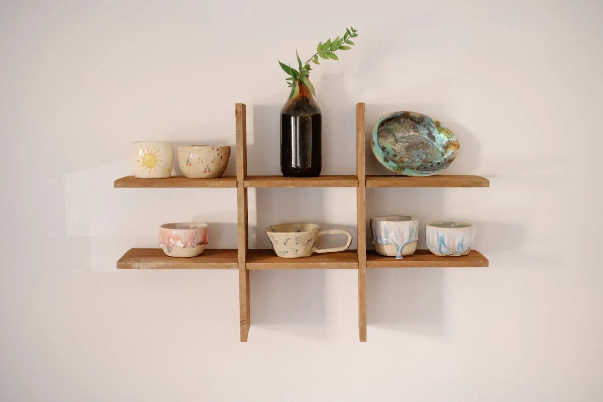 Wood shelf holding handmade ceramics and a branch in a dark bottle