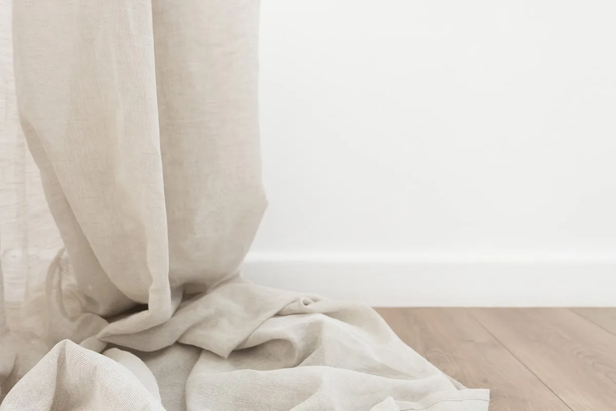 Natural linen curtain pooling on a warm wood floor against a white wall