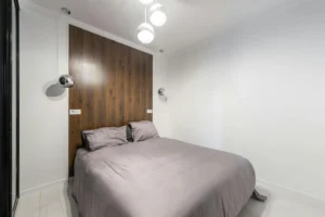 Neatly made bed against a warm wood feature wall in a compact bright bedroom
