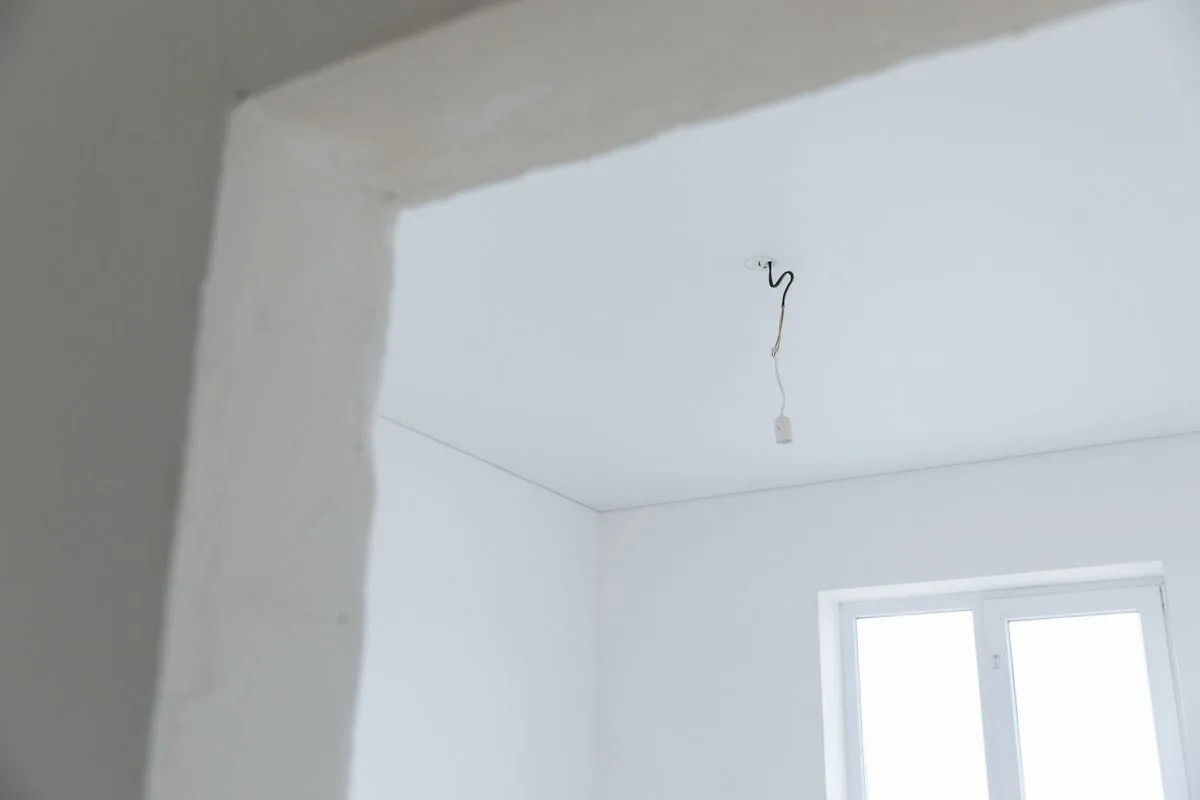 Bare rental room corner showing the white textured ceiling and a single hanging light bulb
