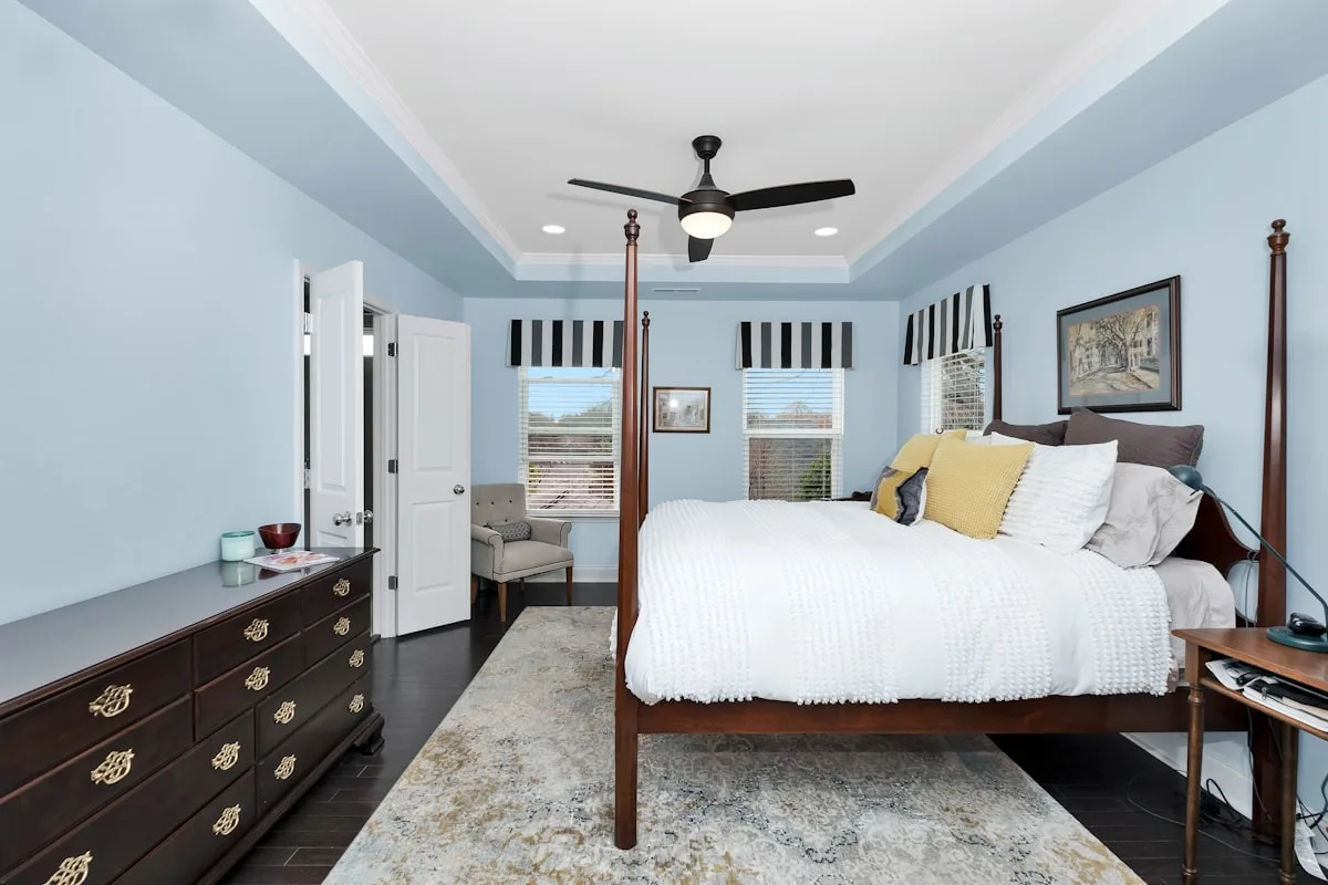 Light blue primary bedroom with a four-poster bed under a tray ceiling and crown molding