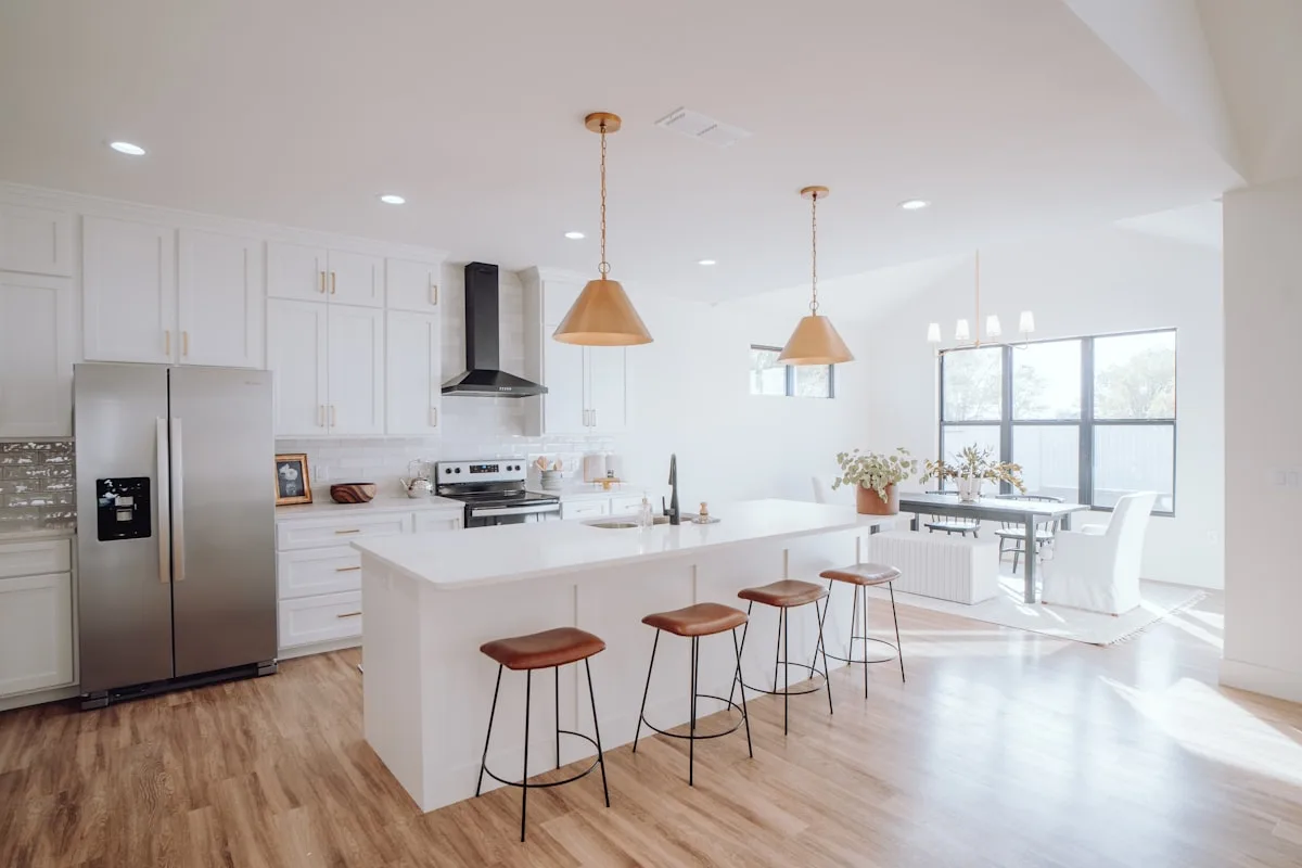Open white kitchen with light wood-look vinyl floor planks, breakfast island and stools