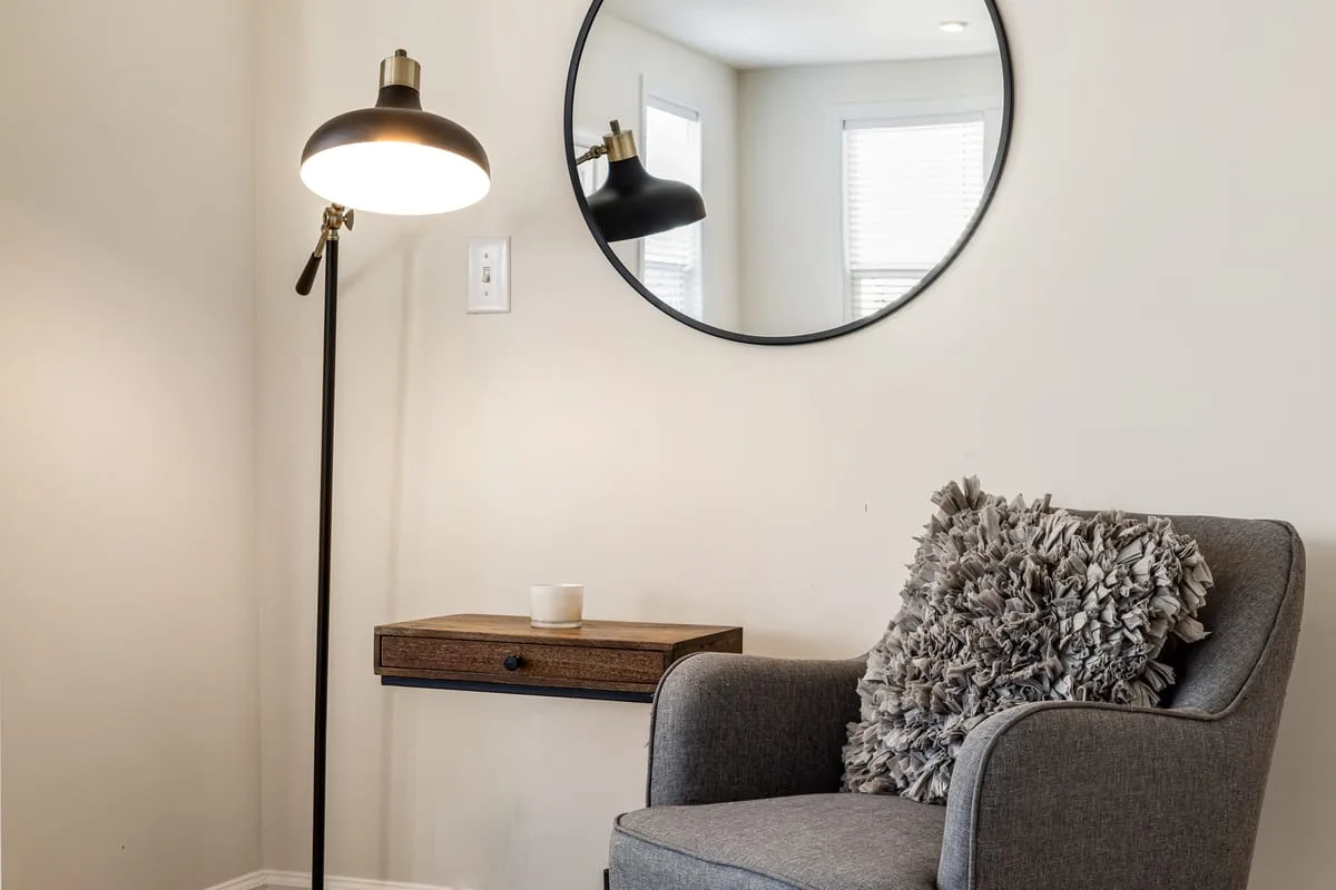Cozy living room corner with a floor lamp, round mirror and gray armchair