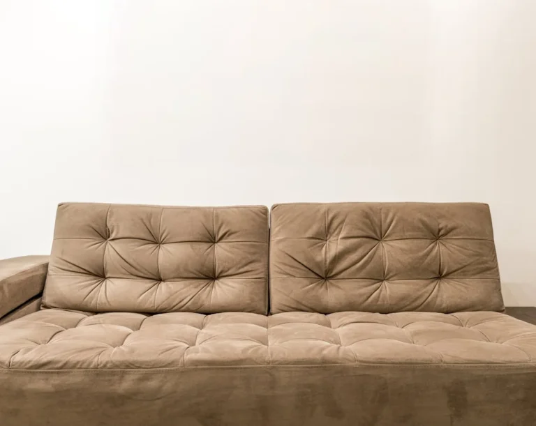 Tan tufted convertible futon sofa against a white wall in a small studio living area