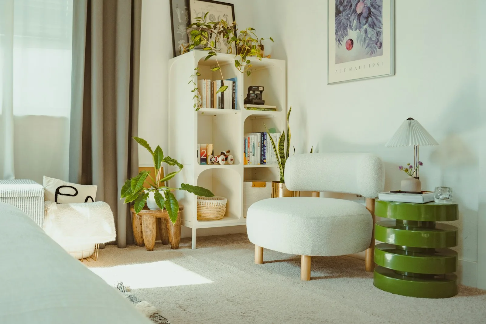 Cozy reading nook in a small apartment with plants, white shelving and a sage green side table in warm natural light