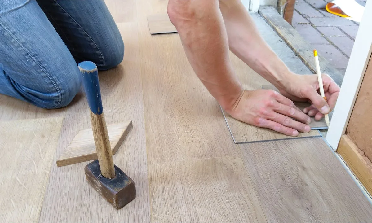Hands installing a peel-and-stick vinyl floor tile in a renter bathroom DIY install