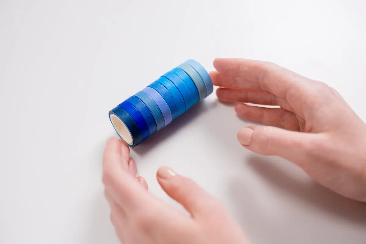 Hands holding a stack of blue washi tape rolls of varying shades